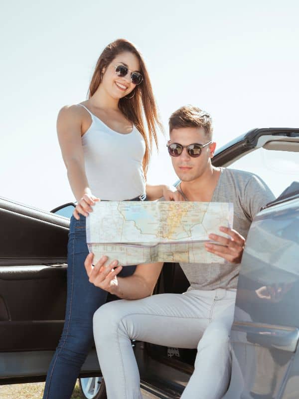 Travelers planning their route with a road map beside a rental car in Paros